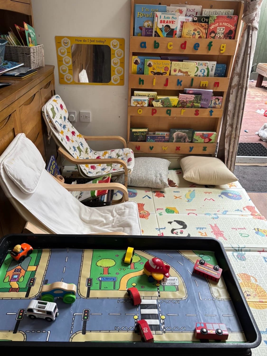 The reading corner — children's bookshelf labelled with the alphabet, two cushioned chairs and a road-mat play table in the foreground